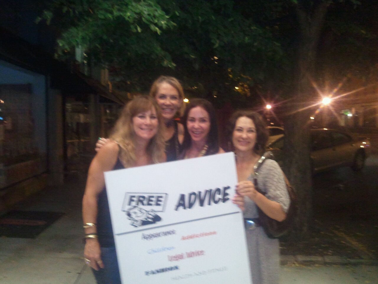 Four Adventure Girls smiling together at night while holding their homemade Free Advice sign.