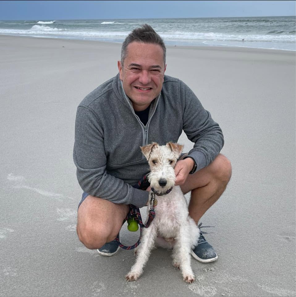 Oz smiling on the beach beside his dog.